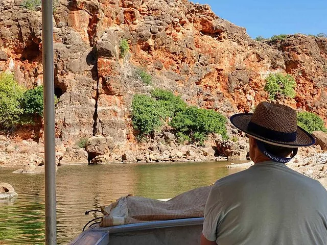 Person in hat on a boat looking at steep red rock cliffs