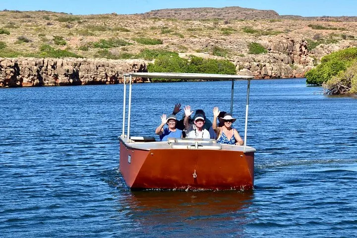Group of people waving from a small boat cruising on a river